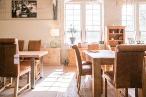 A scene of a section of Ashton & Coleman's Two Dales showroom featuring two dining tables with leather chairs, a bookcase, two sideboards a glass lamp and tall windows of the old mill.