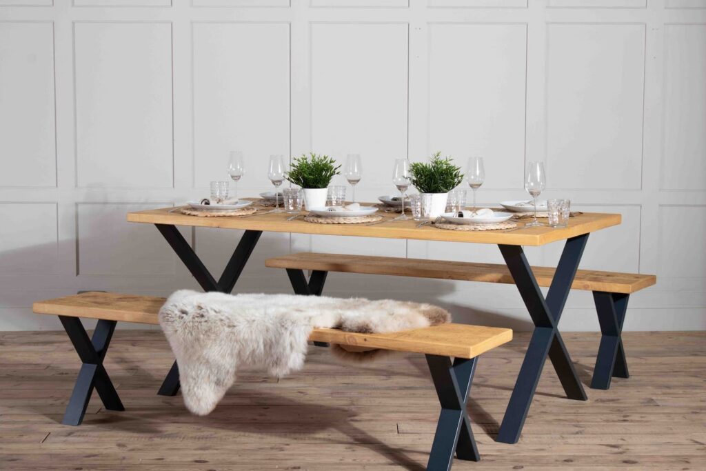 A rustic wooden top table with metal X shaped base is dressed ready for a dinner party with 2 matching benches