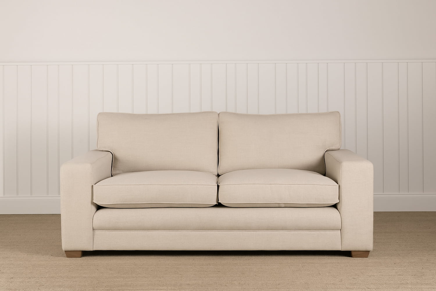 A modern square arm sofa upholstered in pale linen sits on a natural seagrass carpet in front of a off white painted wall with low height off white painted T&G panelling.